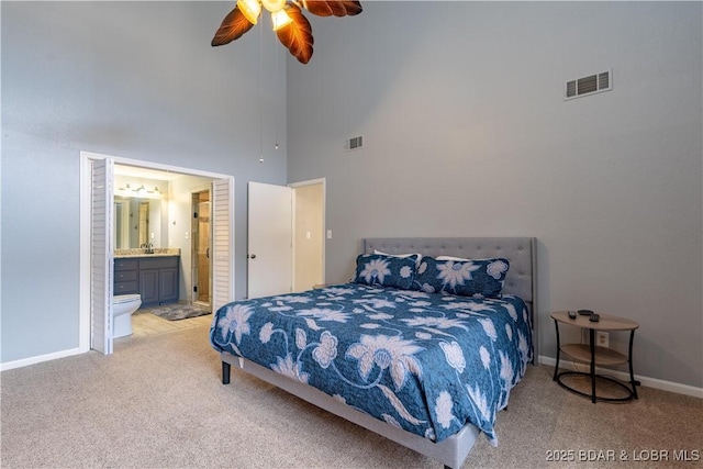 bedroom featuring ceiling fan, ensuite bathroom, carpet floors, and a towering ceiling