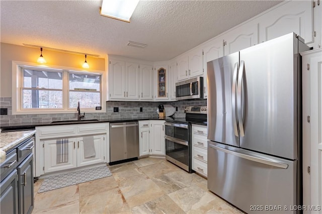 kitchen with appliances with stainless steel finishes, tasteful backsplash, white cabinetry, sink, and a textured ceiling