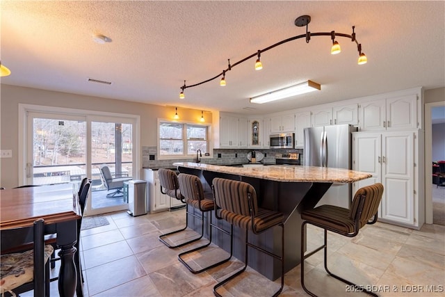 kitchen with white cabinetry, backsplash, stainless steel appliances, light stone countertops, and a kitchen bar