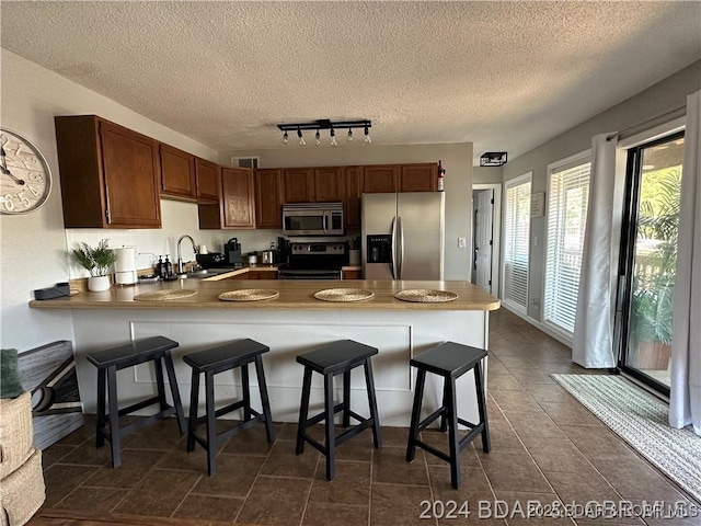 kitchen featuring appliances with stainless steel finishes, a breakfast bar, rail lighting, sink, and kitchen peninsula