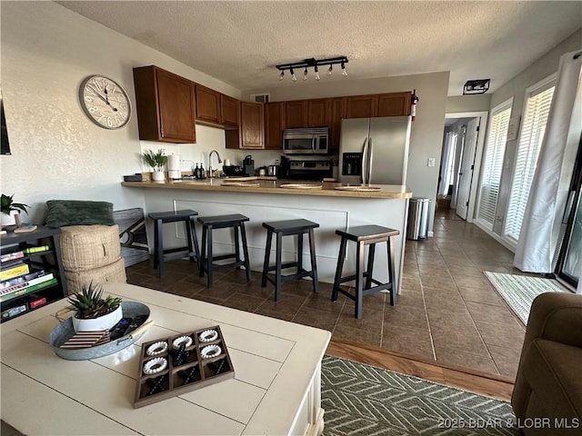 kitchen featuring a breakfast bar, stainless steel appliances, a textured ceiling, dark tile patterned flooring, and kitchen peninsula