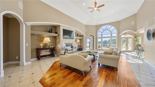 living room with a stone fireplace, a towering ceiling, light tile patterned floors, ceiling fan, and french doors