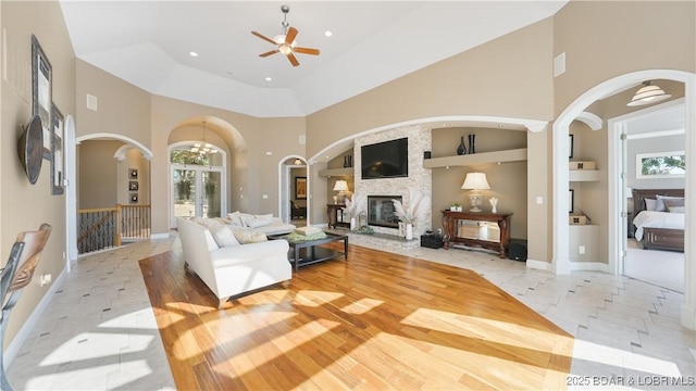 living room featuring light tile patterned floors, a stone fireplace, ceiling fan, a high ceiling, and built in shelves