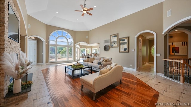 living room with ceiling fan, a towering ceiling, and light hardwood / wood-style flooring