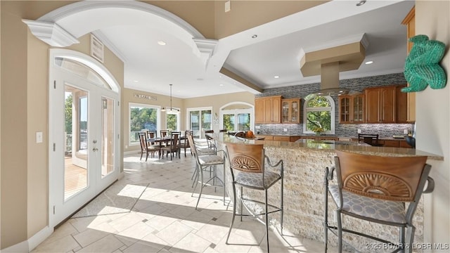 kitchen with french doors, a kitchen bar, stone countertops, a wealth of natural light, and decorative backsplash