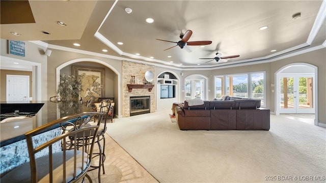 living room with a raised ceiling, ornamental molding, a large fireplace, and light colored carpet