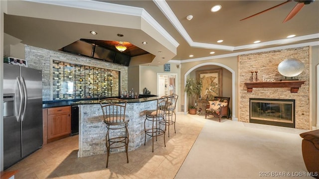 kitchen with a breakfast bar area, a tray ceiling, a fireplace, ornamental molding, and stainless steel fridge with ice dispenser