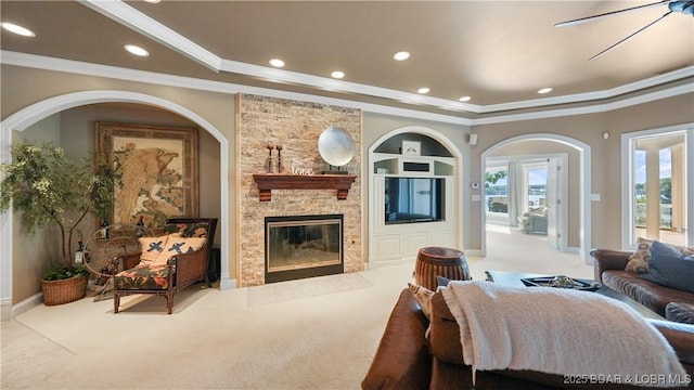 living room with crown molding, a stone fireplace, light carpet, and built in shelves