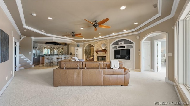 carpeted living room with ornamental molding, a fireplace, built in features, and a raised ceiling