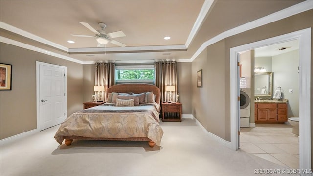 bedroom featuring washer / clothes dryer, a tray ceiling, ensuite bath, and ceiling fan