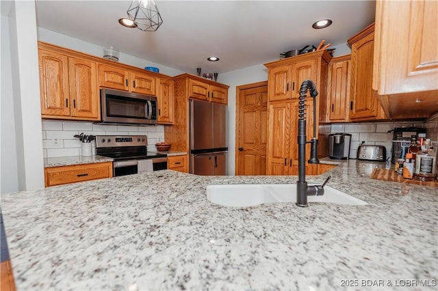 kitchen with sink, stainless steel appliances, light stone countertops, decorative backsplash, and decorative light fixtures