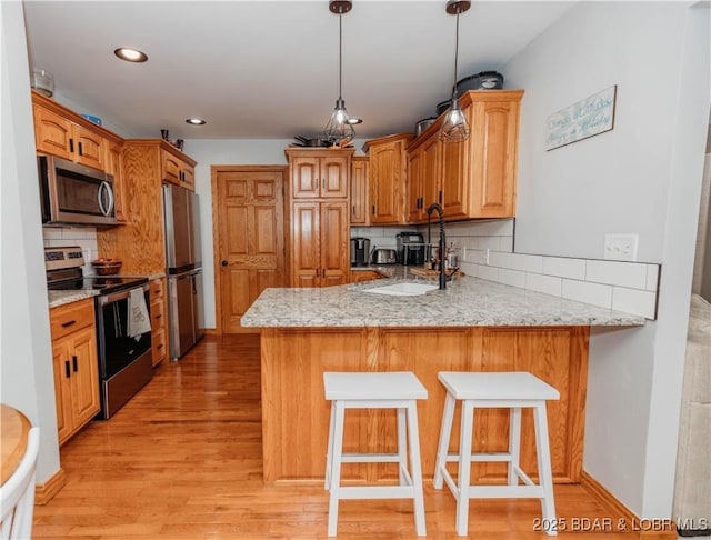 kitchen with light stone counters, a breakfast bar area, stainless steel appliances, and kitchen peninsula