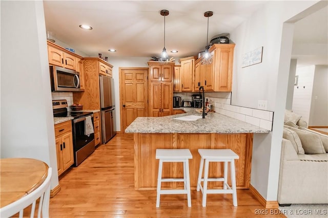 kitchen with sink, kitchen peninsula, stainless steel appliances, light stone countertops, and light wood-type flooring