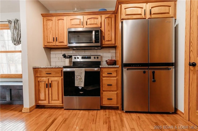 kitchen with stainless steel appliances, light stone countertops, backsplash, and light hardwood / wood-style floors