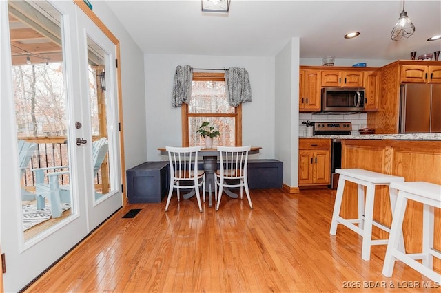 kitchen featuring stainless steel appliances, light hardwood / wood-style floors, hanging light fixtures, and backsplash