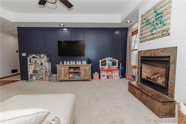 living room featuring ceiling fan, a fireplace, a tray ceiling, and carpet floors