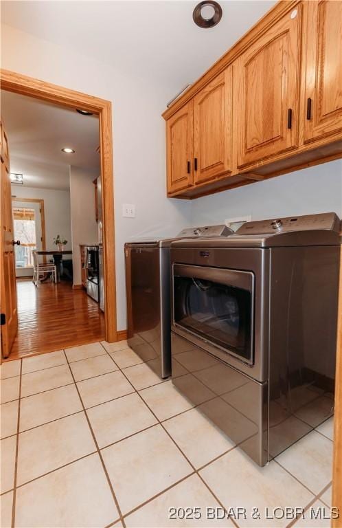 clothes washing area with washer and dryer, light tile patterned floors, and cabinets