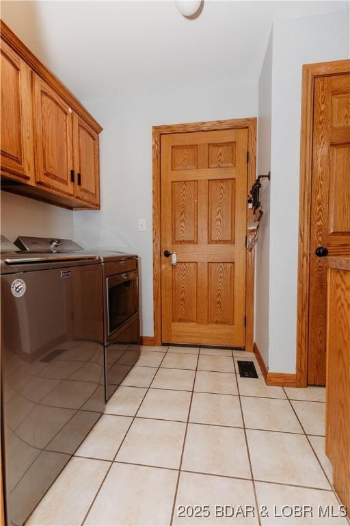 clothes washing area featuring cabinets, washing machine and dryer, and light tile patterned floors