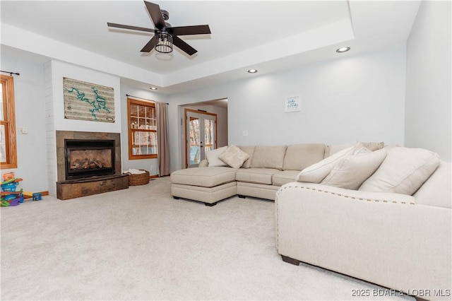 carpeted living room featuring a tray ceiling, a tile fireplace, french doors, and ceiling fan