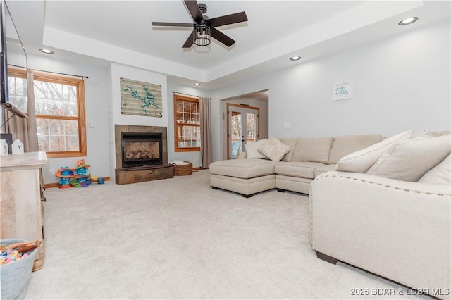 carpeted living room featuring a tray ceiling, a fireplace, and ceiling fan