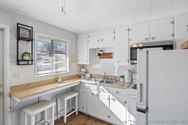 kitchen featuring sink, white appliances, white cabinetry, a kitchen bar, and decorative backsplash