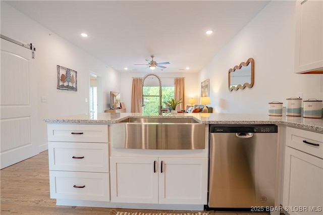 kitchen with sink, dishwasher, ceiling fan, a barn door, and white cabinets