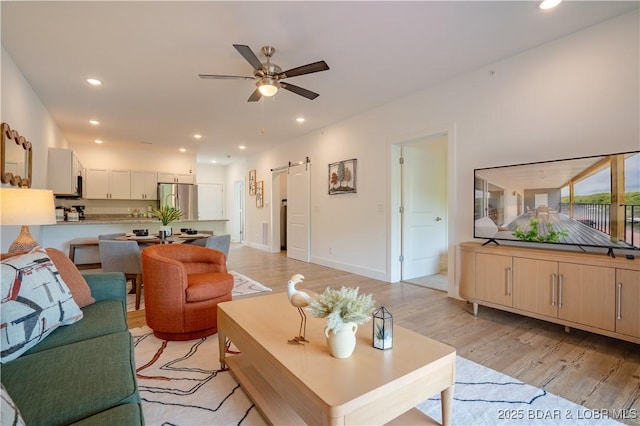 living room with light hardwood / wood-style flooring, a barn door, and ceiling fan