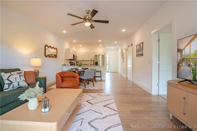 living room with a barn door, ceiling fan, and light wood-type flooring