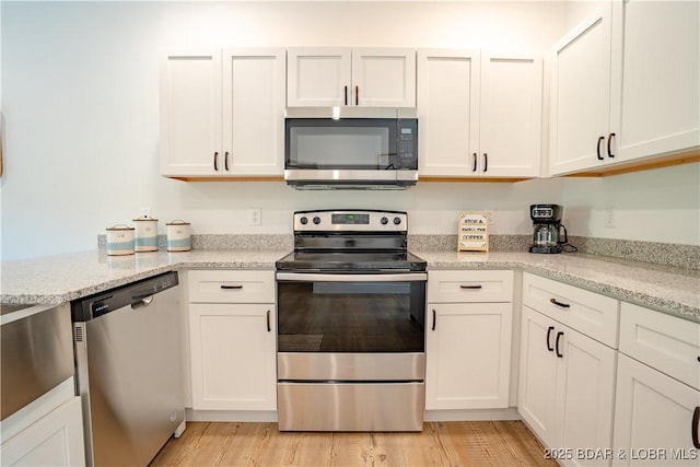 kitchen with light stone counters, stainless steel appliances, light wood-type flooring, and white cabinets