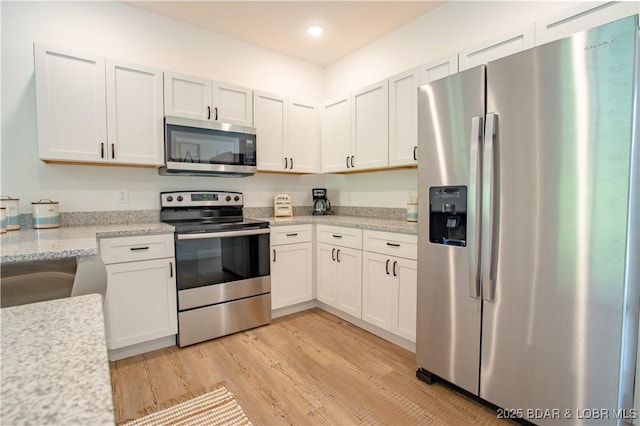 kitchen featuring appliances with stainless steel finishes, sink, white cabinets, light hardwood / wood-style floors, and light stone countertops