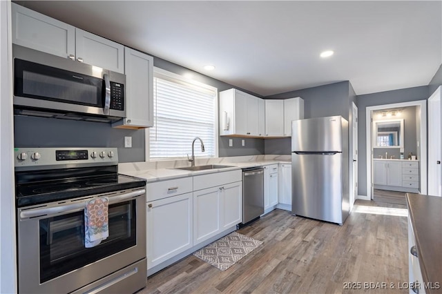 kitchen featuring sink, light hardwood / wood-style flooring, appliances with stainless steel finishes, light stone countertops, and white cabinets