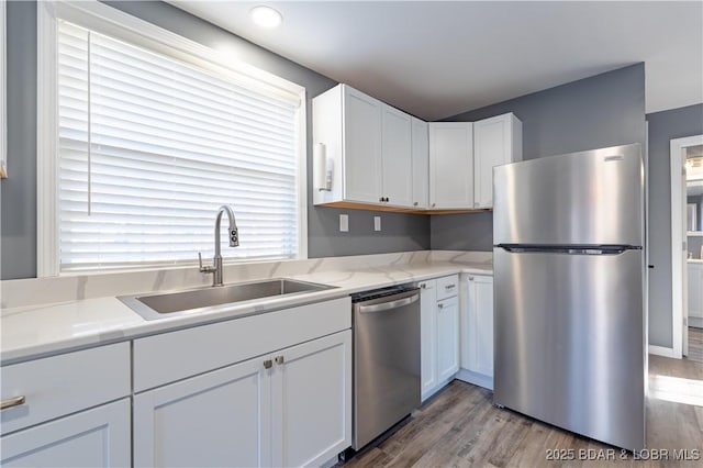 kitchen with appliances with stainless steel finishes, white cabinetry, sink, light stone countertops, and light wood-type flooring