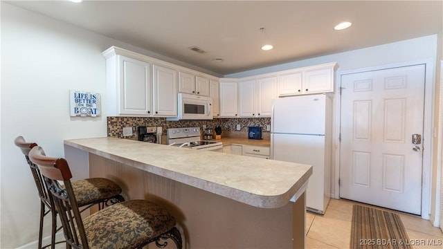 kitchen featuring a breakfast bar area, white cabinets, white appliances, and kitchen peninsula