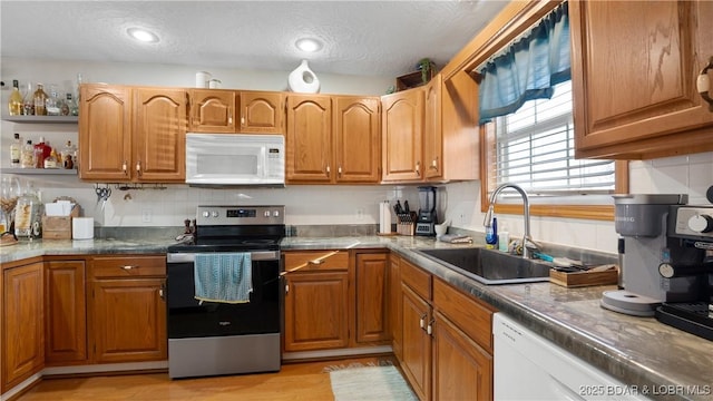 kitchen featuring sink, a textured ceiling, light wood-type flooring, white appliances, and backsplash