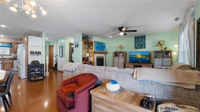 living room with hardwood / wood-style floors, ceiling fan with notable chandelier, and sink