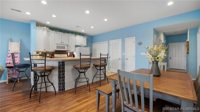 kitchen with a breakfast bar, backsplash, white cabinets, light hardwood / wood-style floors, and white appliances