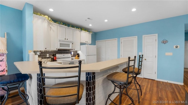 kitchen featuring a breakfast bar, white cabinets, dark hardwood / wood-style flooring, kitchen peninsula, and white appliances