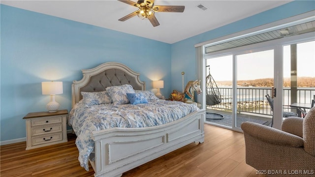 bedroom with access to outside, light hardwood / wood-style floors, ceiling fan, and a water view