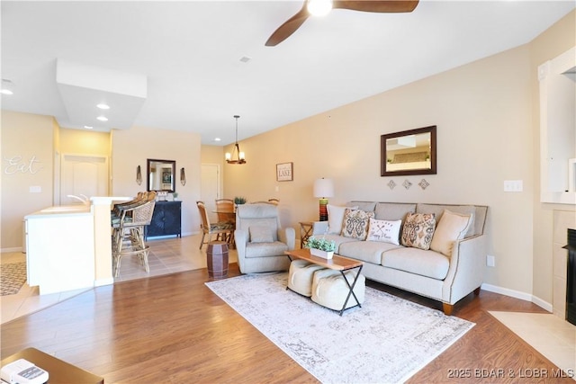 living room with hardwood / wood-style flooring, a fireplace, and ceiling fan with notable chandelier