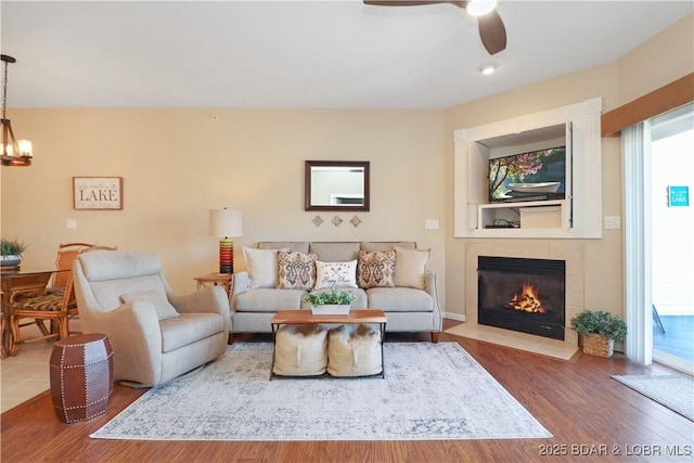 living room with wood-type flooring, plenty of natural light, ceiling fan with notable chandelier, and a fireplace