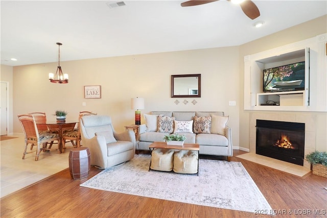 living room featuring a tiled fireplace, hardwood / wood-style floors, and ceiling fan with notable chandelier