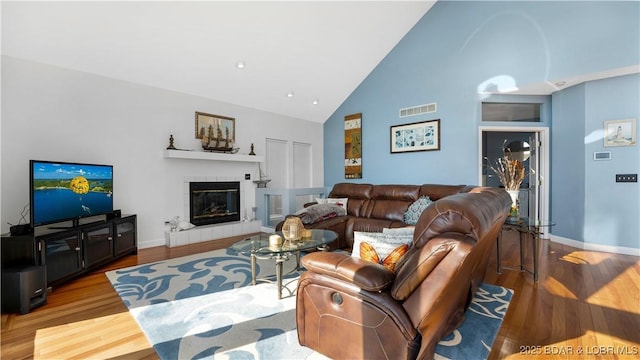 living room featuring hardwood / wood-style flooring, high vaulted ceiling, and a tile fireplace