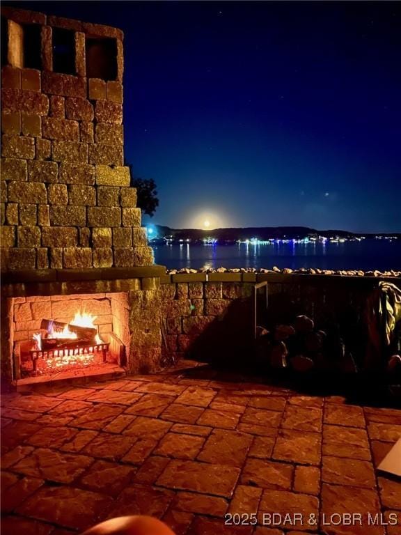 patio at night with a water view and a fireplace