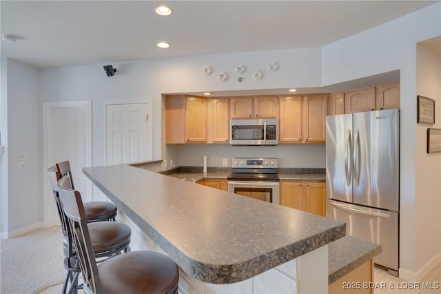 kitchen with stainless steel appliances, a kitchen breakfast bar, and light brown cabinetry