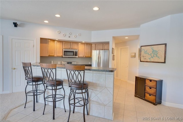 kitchen with a kitchen breakfast bar, light tile patterned floors, kitchen peninsula, stainless steel appliances, and light brown cabinets