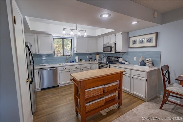 kitchen featuring pendant lighting, stainless steel appliances, tasteful backsplash, white cabinets, and a raised ceiling