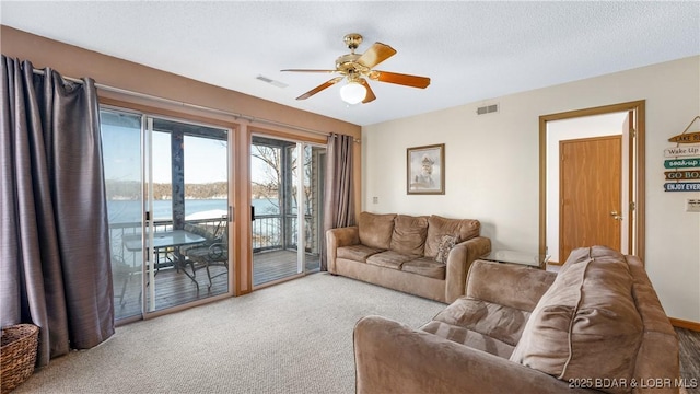 living room featuring a textured ceiling, light colored carpet, ceiling fan, and a water view