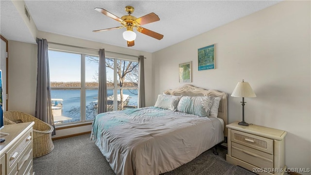 bedroom featuring a water view, ceiling fan, a textured ceiling, and dark colored carpet