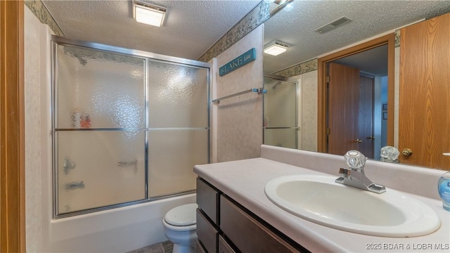 full bathroom with bath / shower combo with glass door, vanity, a textured ceiling, and toilet