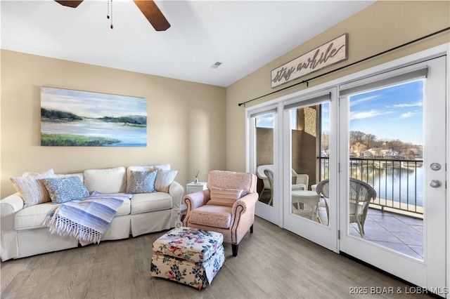 living room with ceiling fan, a water view, and light hardwood / wood-style floors